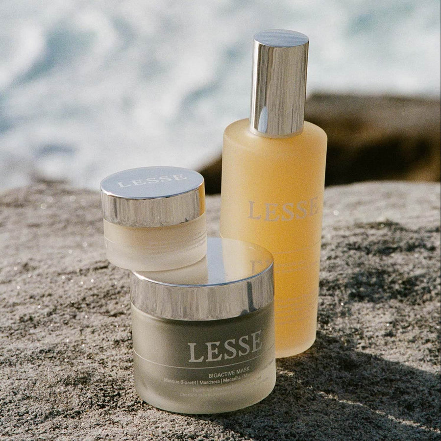 Three skincare products with 'LESSE' branding on a stone surface near water.