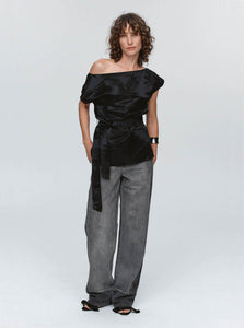 Woman wearing a black off-shoulder top and gray pants on a white background